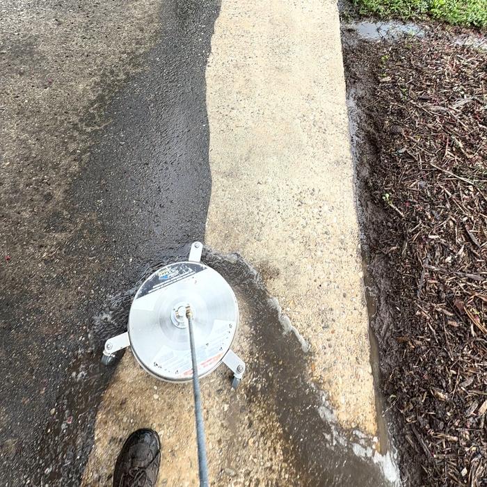 A surface cleaner part-way down a Charlotte walkway. The strip already passed over is pale, clean concrete; the strip beside it is still grey with dirt.