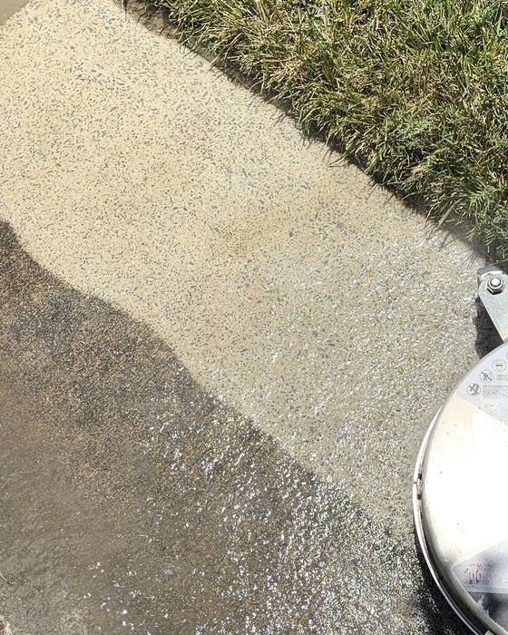A walkway beside a lawn during cleaning. The surface cleaner sits at the edge of the freshly washed section, which is noticeably lighter than the rest.